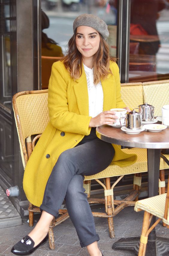 femeie care pe scaun la masă cu bonetă gri și palton galben